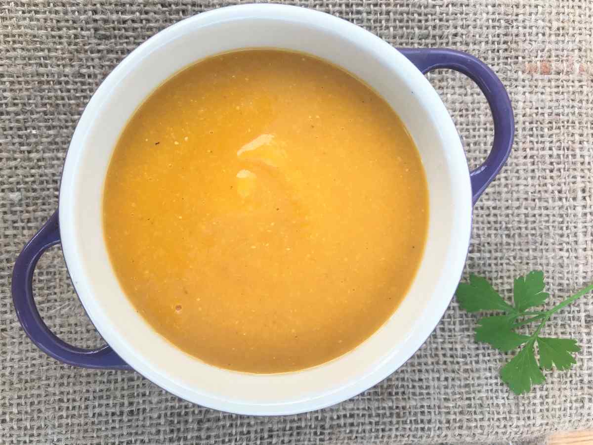 Red lentil and butternut squash soup in bowl on hessian with parsley