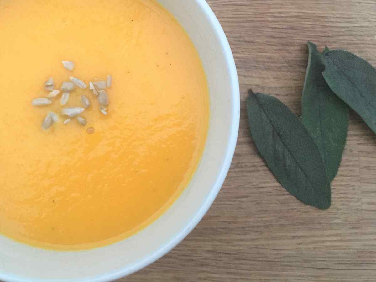 Carrot and apple soup in a bowl with sunflower seeds and sage leaves.