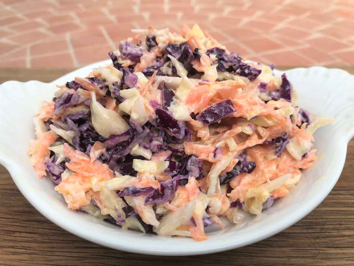 Healthy coleslaw in white dish on wooden board.