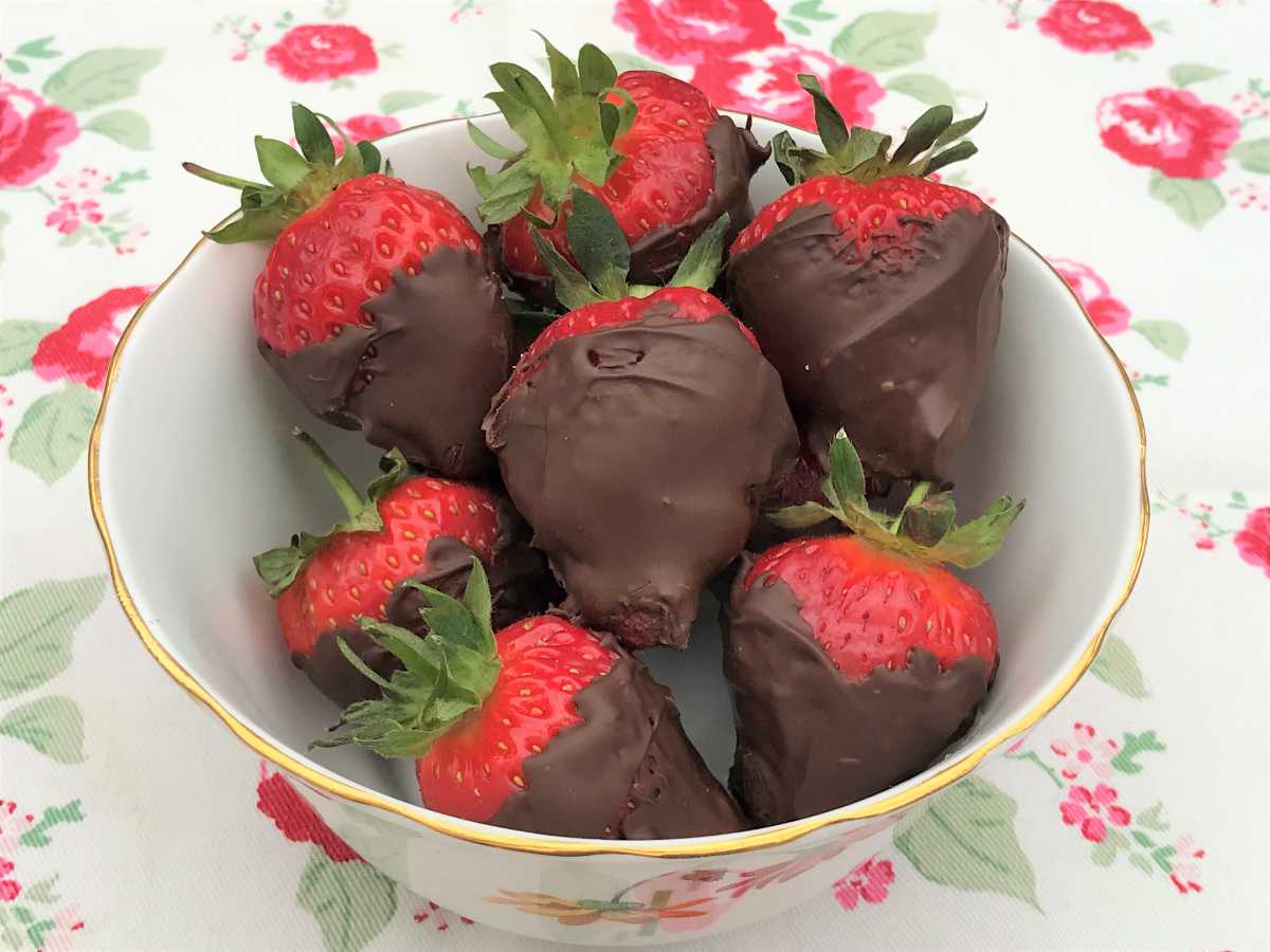 Dark chocolate coated strawberries in a bowl on flowered background