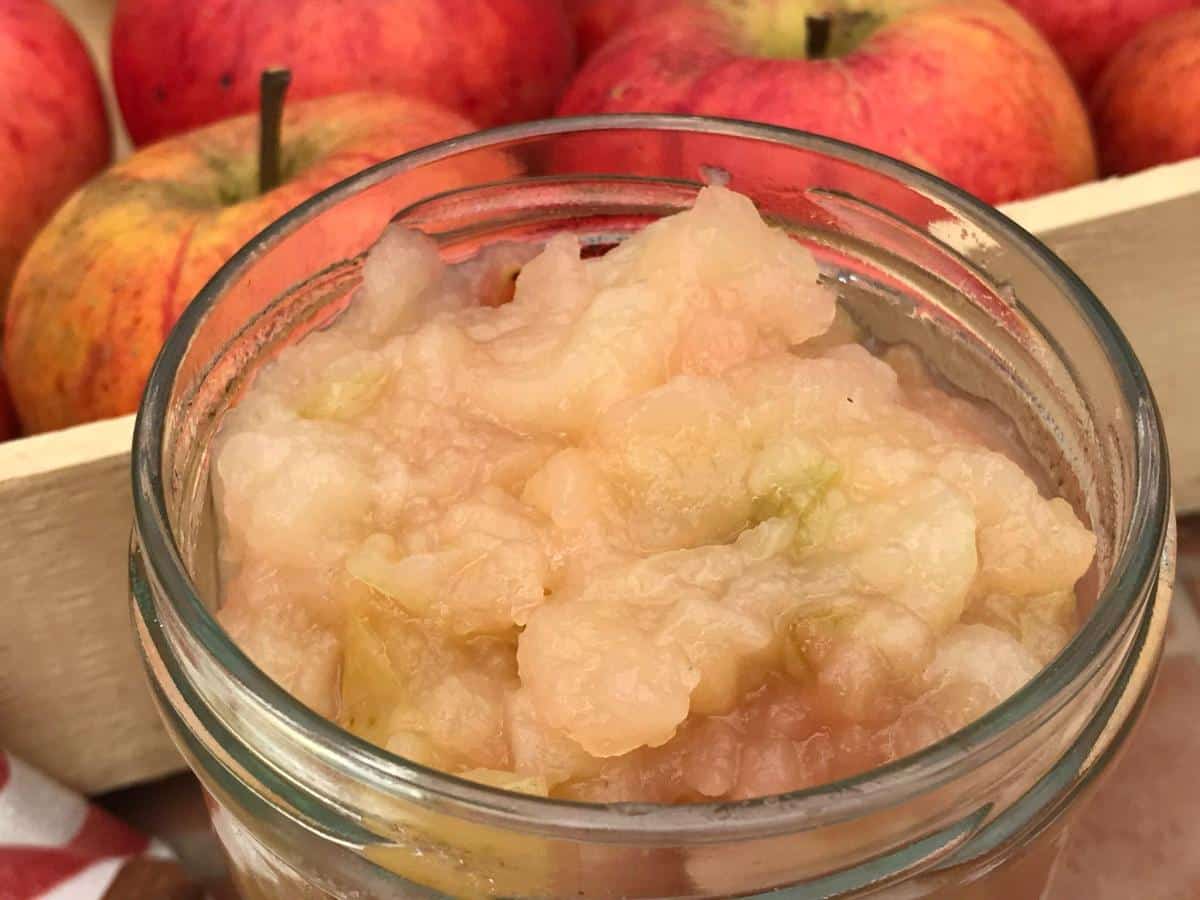 Jar of slow cooker applesauce with apple crate behind.