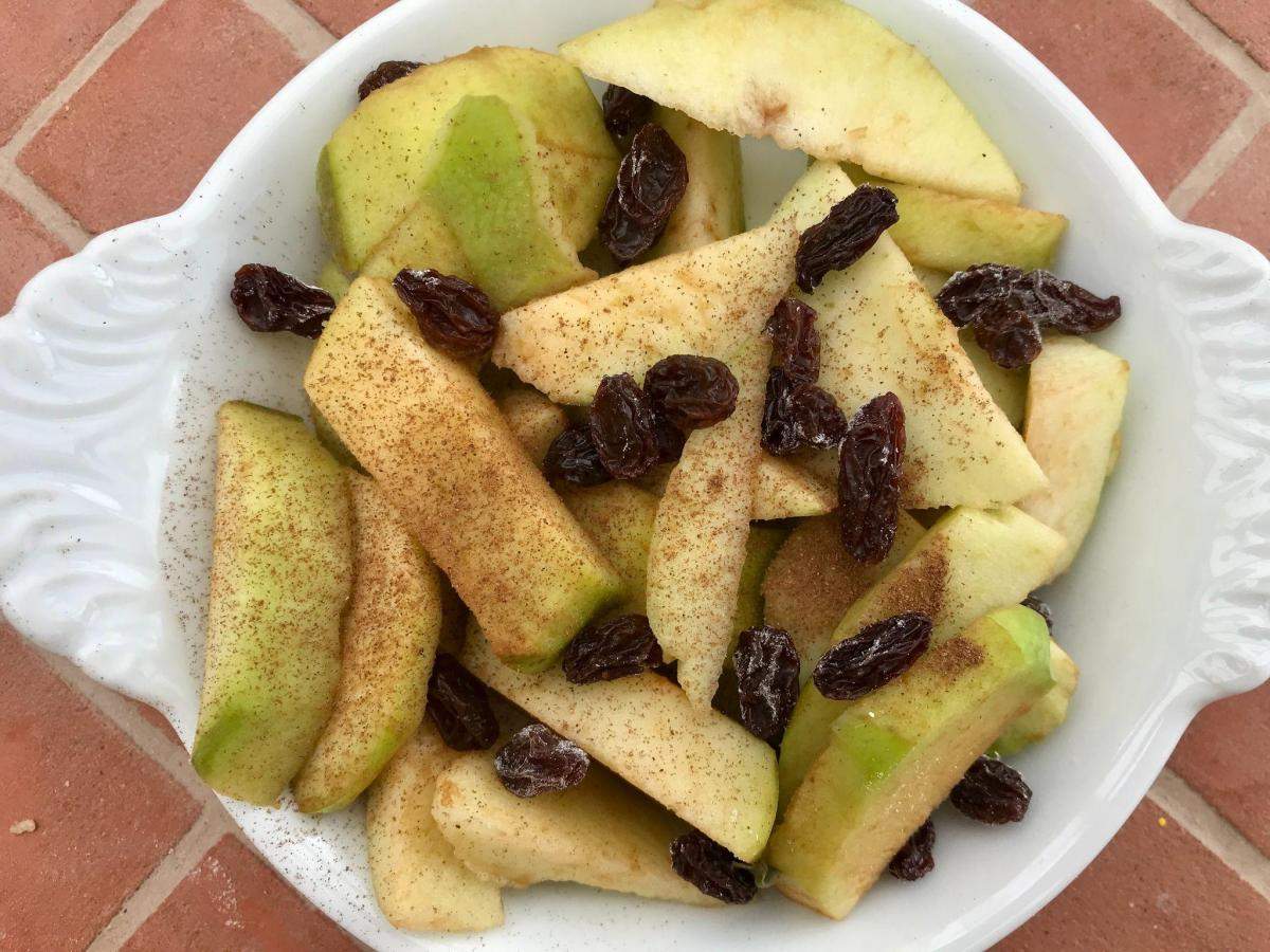 Apple, raisins and cinnamon in baking dish.