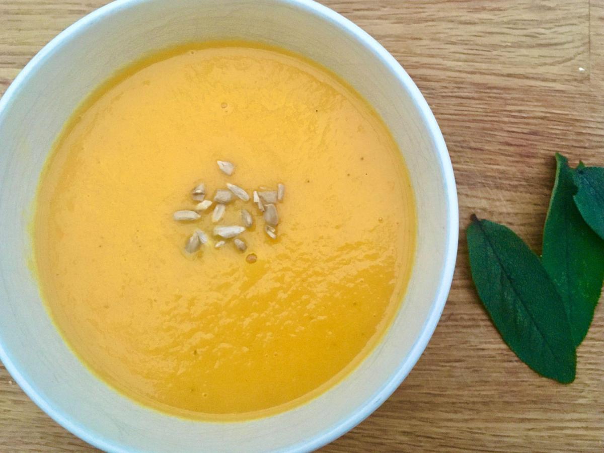Carrot soup with apple and sage in white bowl.