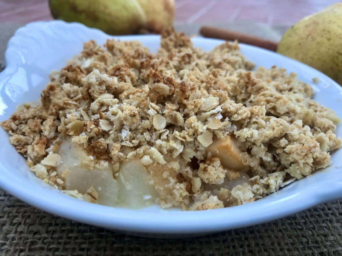 Pear crumble in white dish with pears behind.