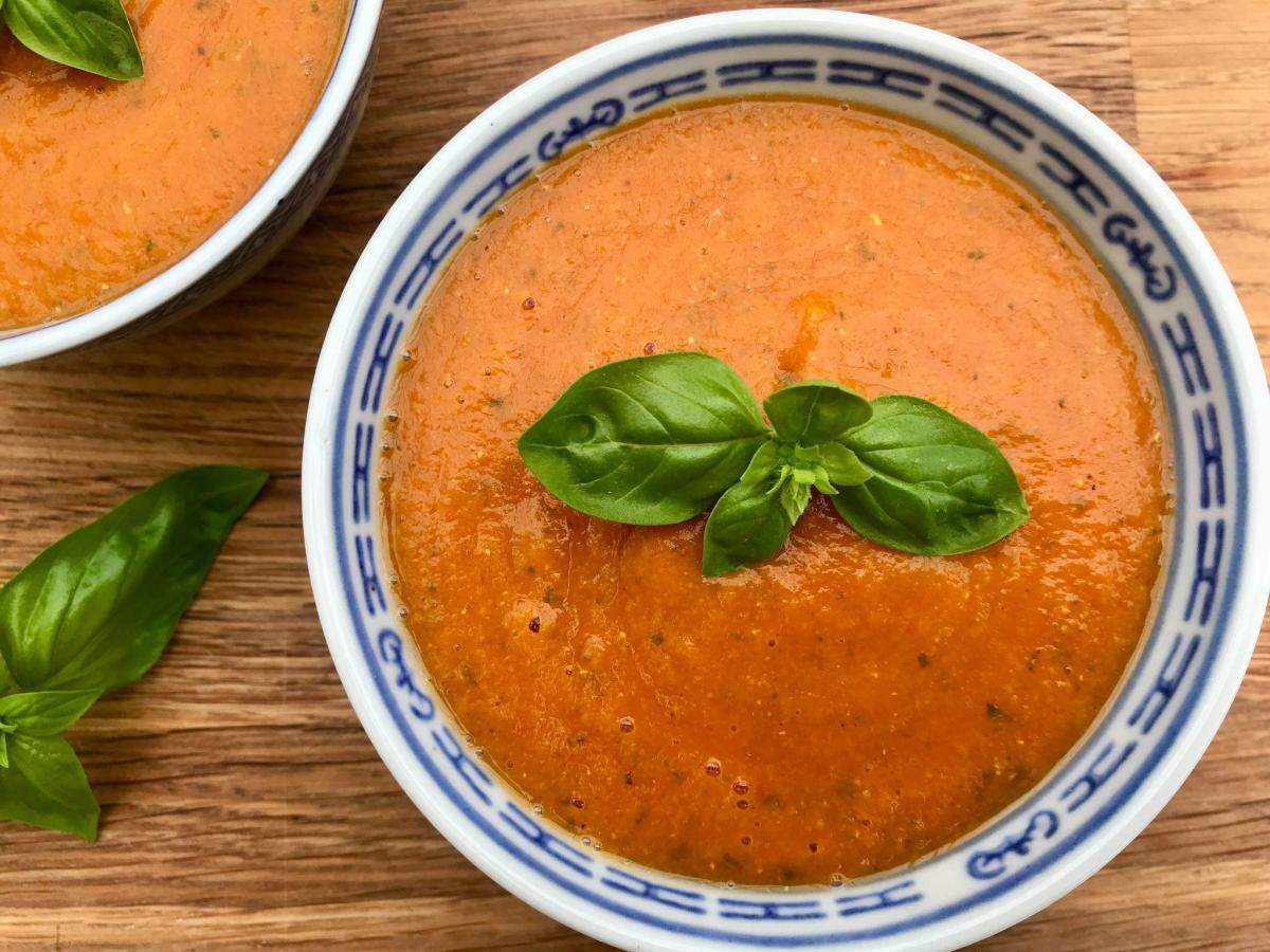 Tomato and red lentil soup with basil on wooden board.