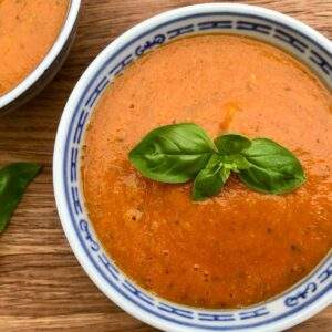 Tomato and red lentil soup with basil on wooden board.