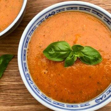 Tomato and red lentil soup with basil on wooden board.