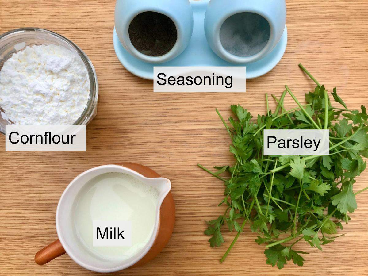 Cornflour, milk, seasoning, parsley on wooden board.