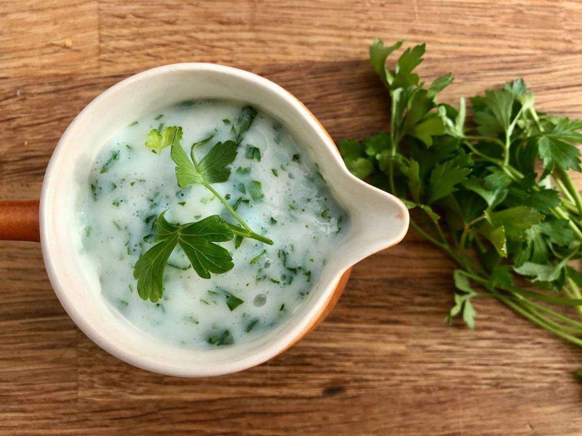 Jug of gluten free parsley sauce with parsley on wooden board.