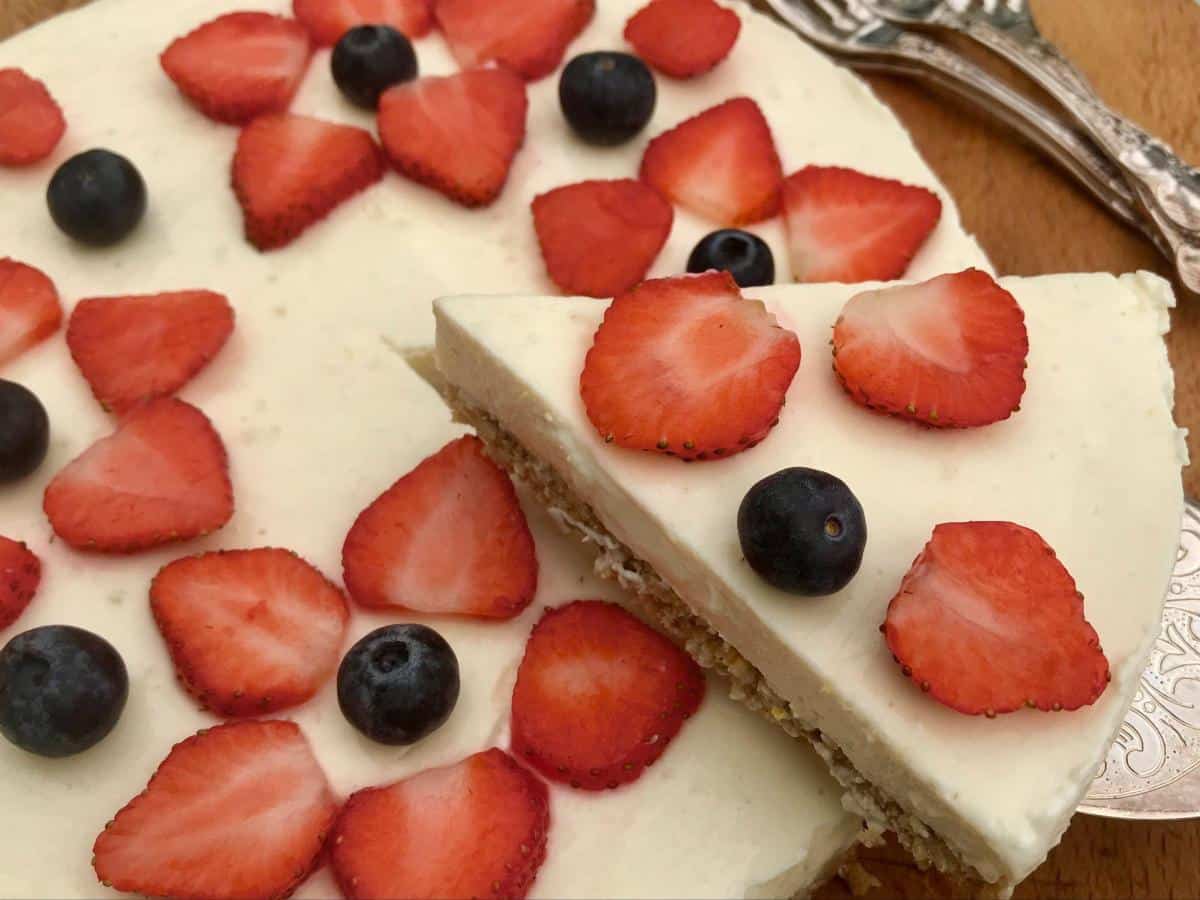 Low fat lemon cheesecake decorated with berries with slice taken out.