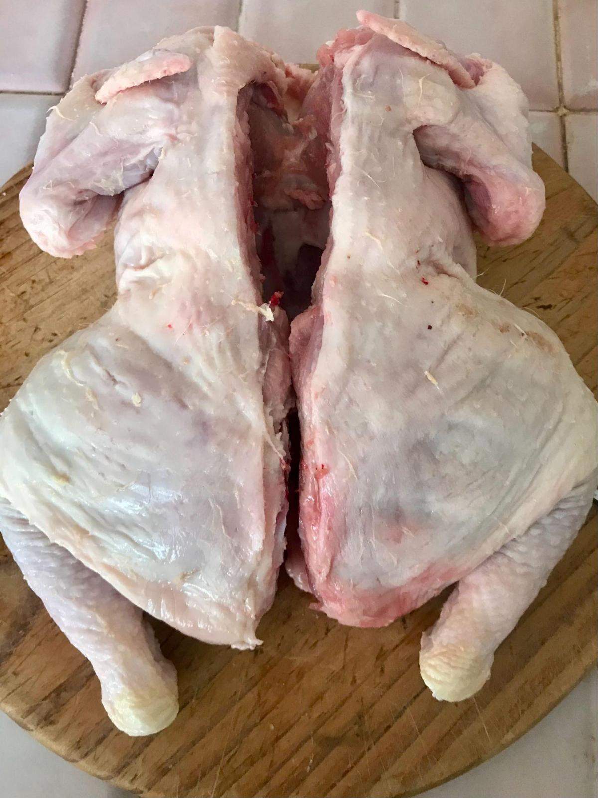 Chicken with backbone removed on wooden board.