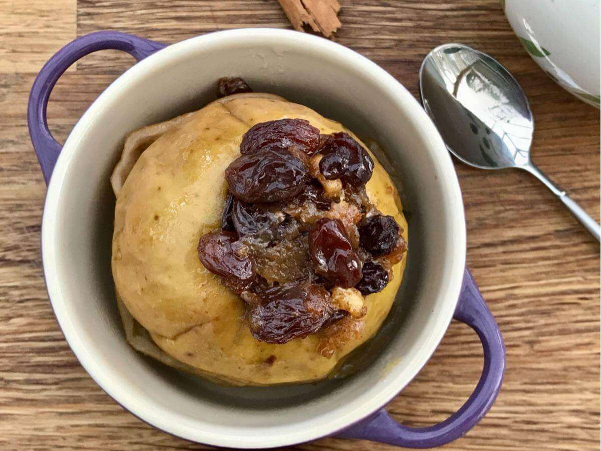 Baked apple with mincemeat in purple handled dish.