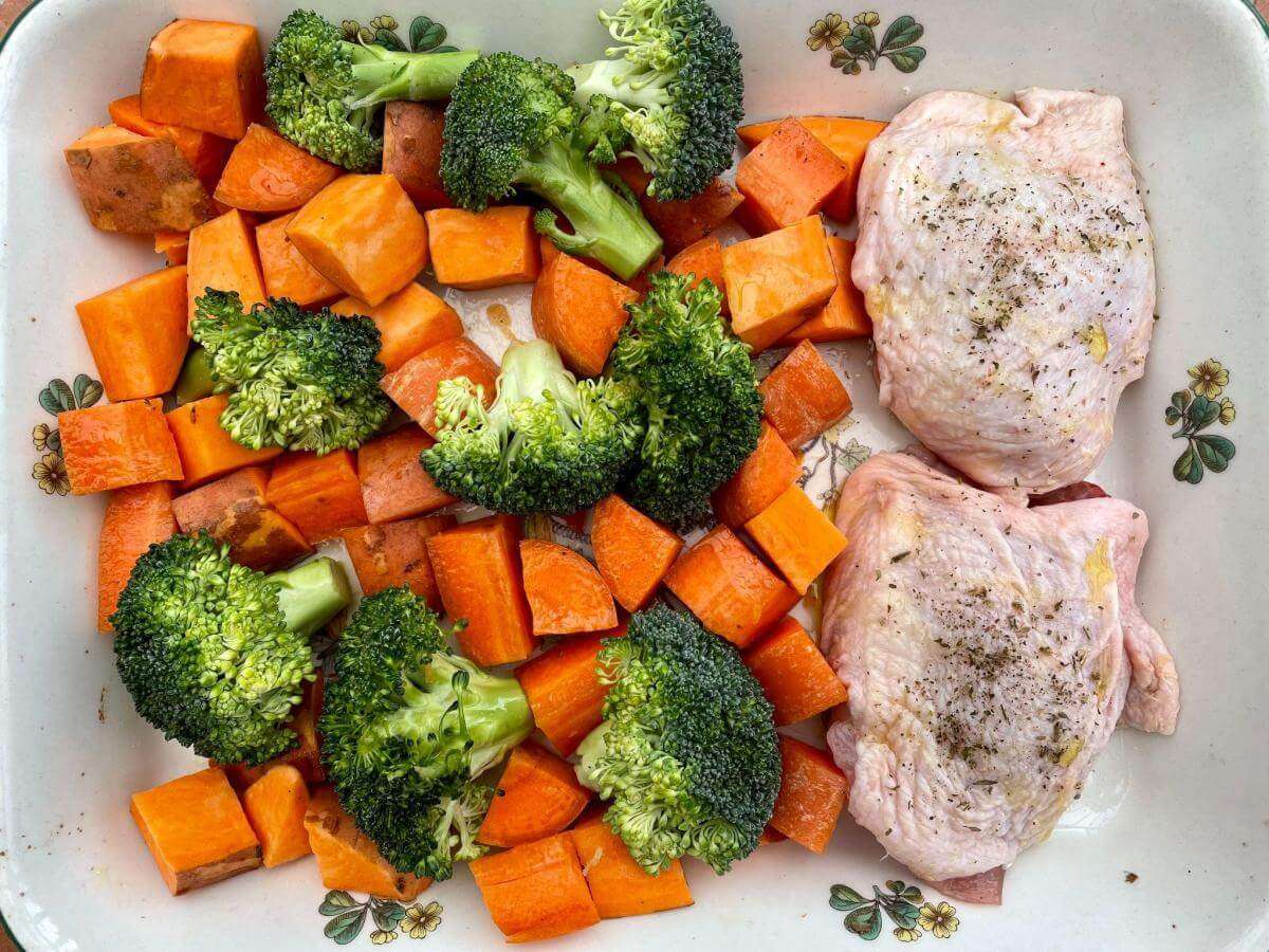 Chicken thighs, sweet potatoes, carrot and broccoli in baking dish.
