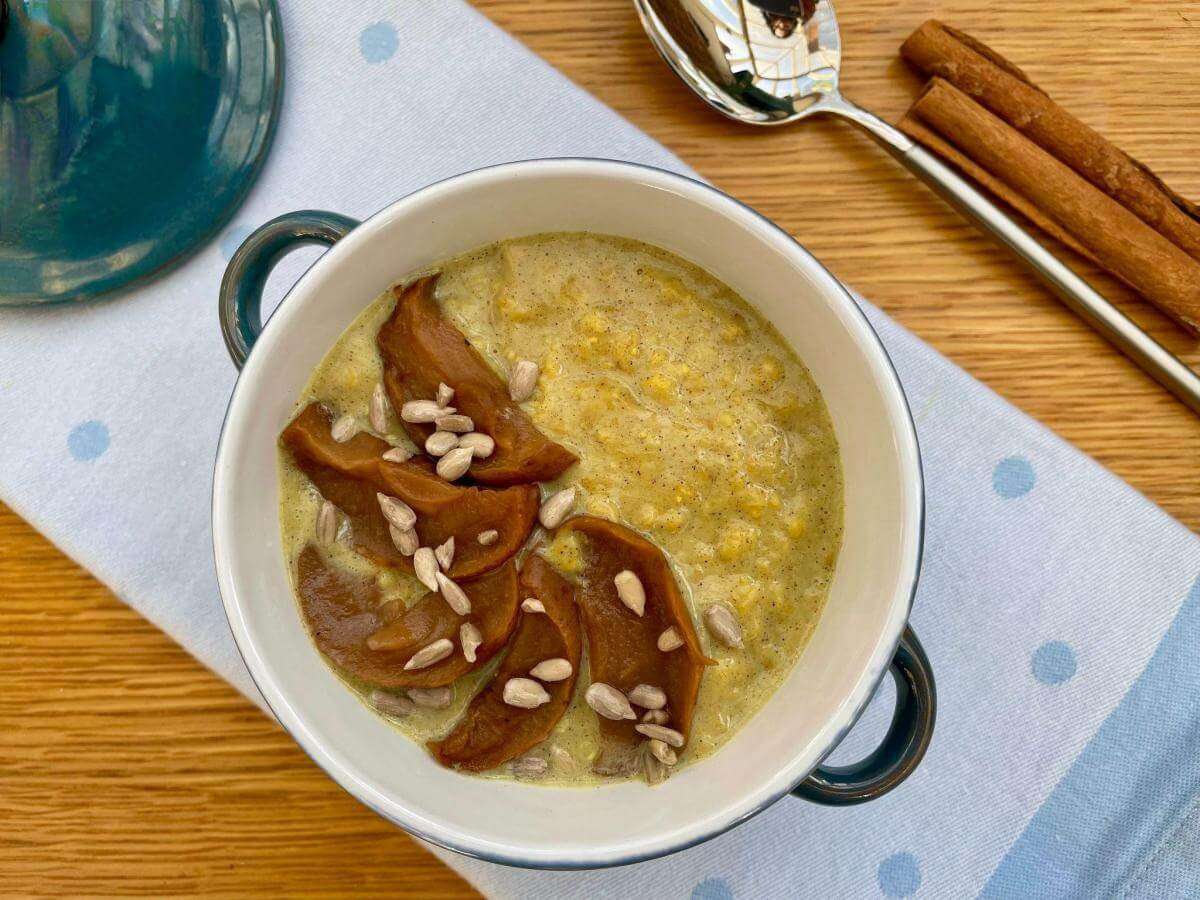 Spiced porridge in bowl with apple and cinnamon sticks.