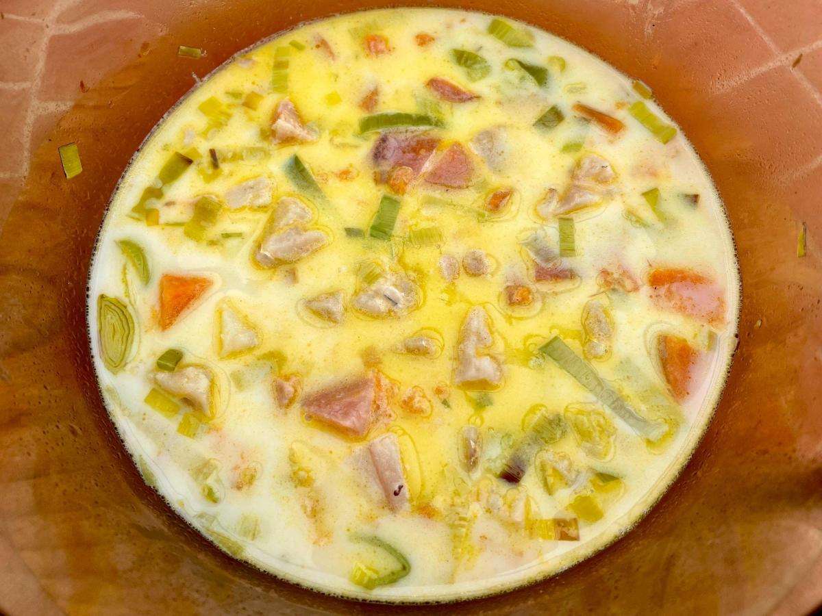 Vegetables and fish in milk in pan.