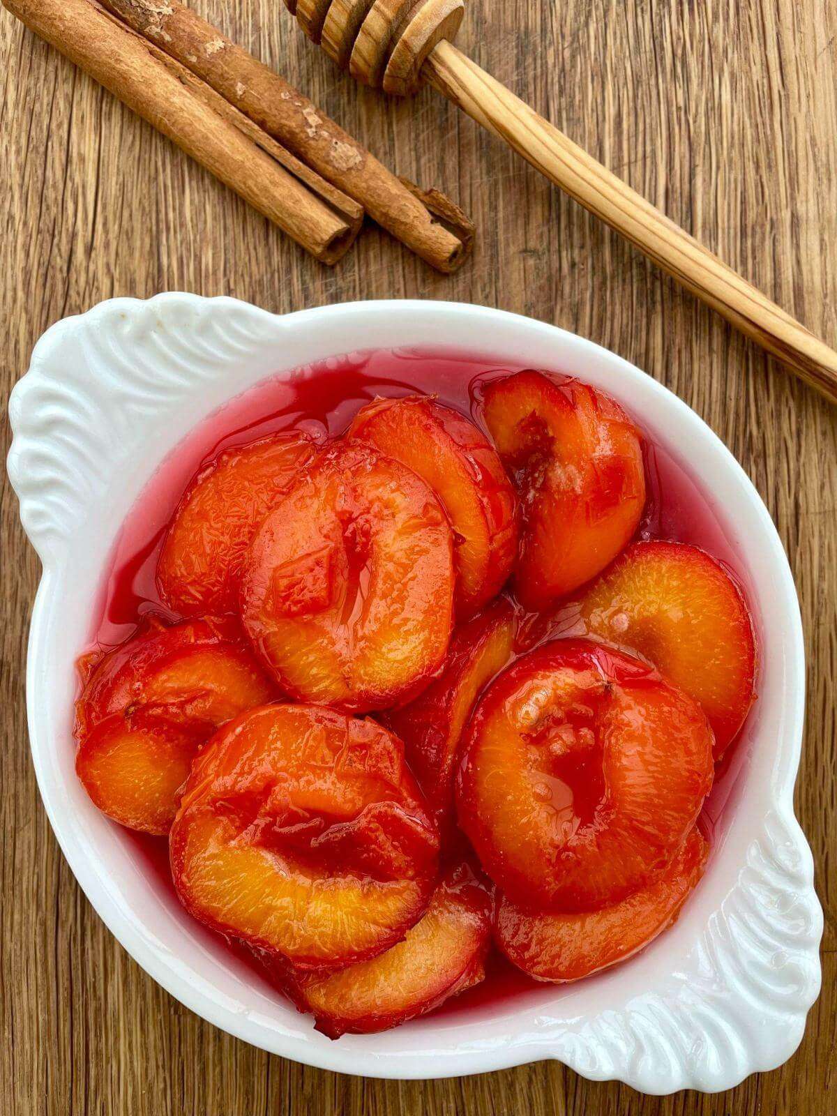 Stewed plums with cinnamon and honey in white bowl.