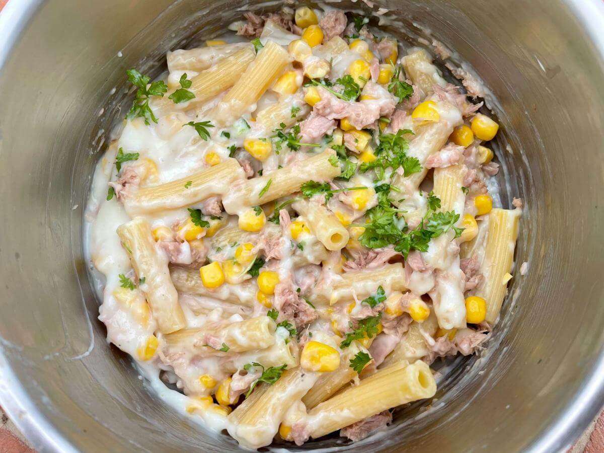 Pasta, tuna and sweetcorn in sauce in pan with parsley.