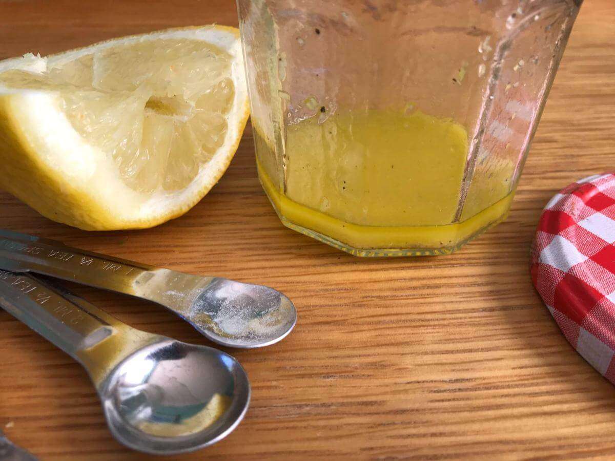Lemon dressing in jug with lemon alongside.