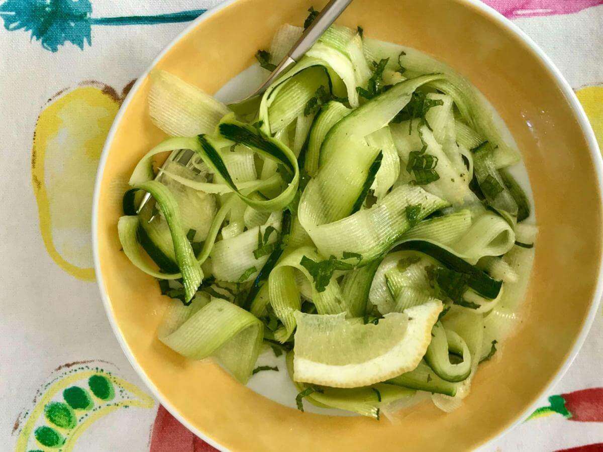 Raw courgette salad in yellow bowl.