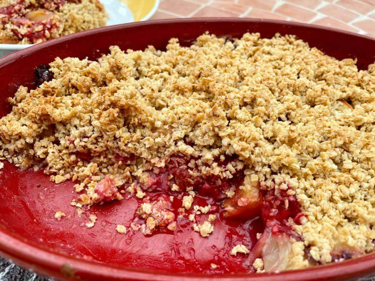 Peach crumble with raspberries in red dish.