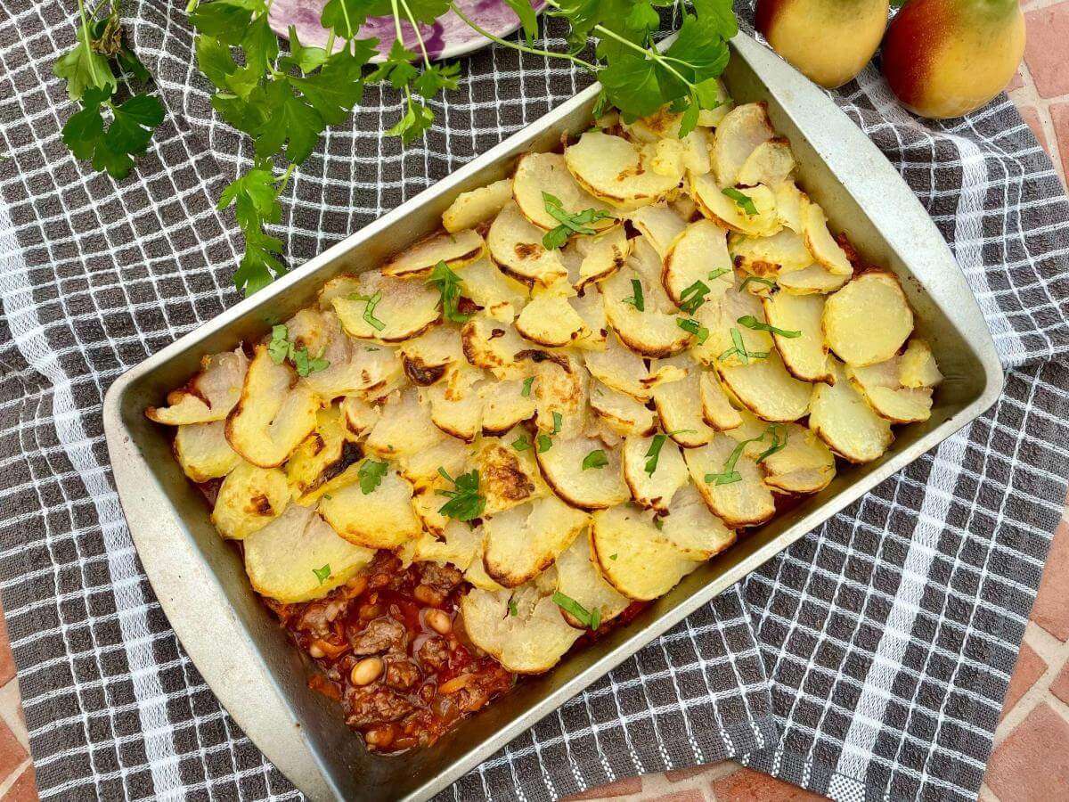 Beef and bean hotpot in metal tray on checked cloth.