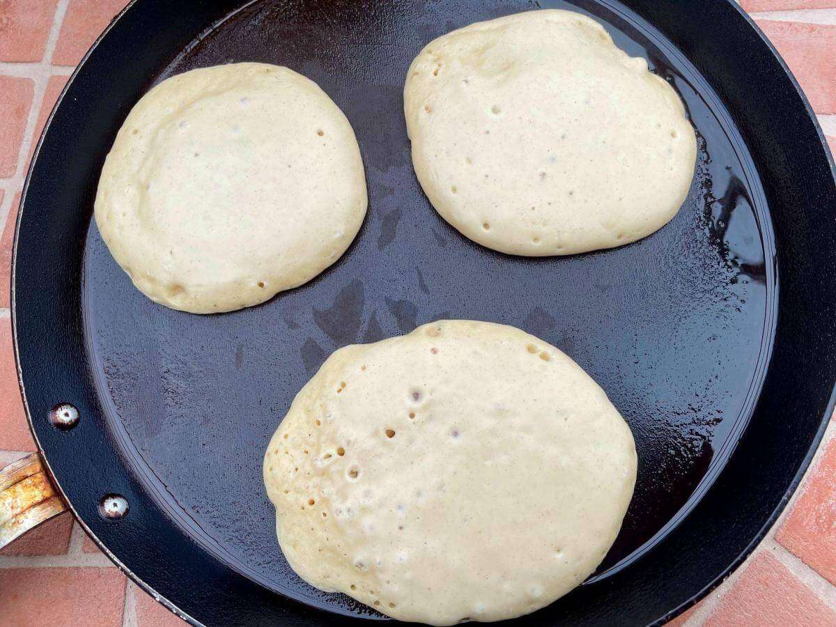 Thick fluffy oat milk pancakes cooking in pan.