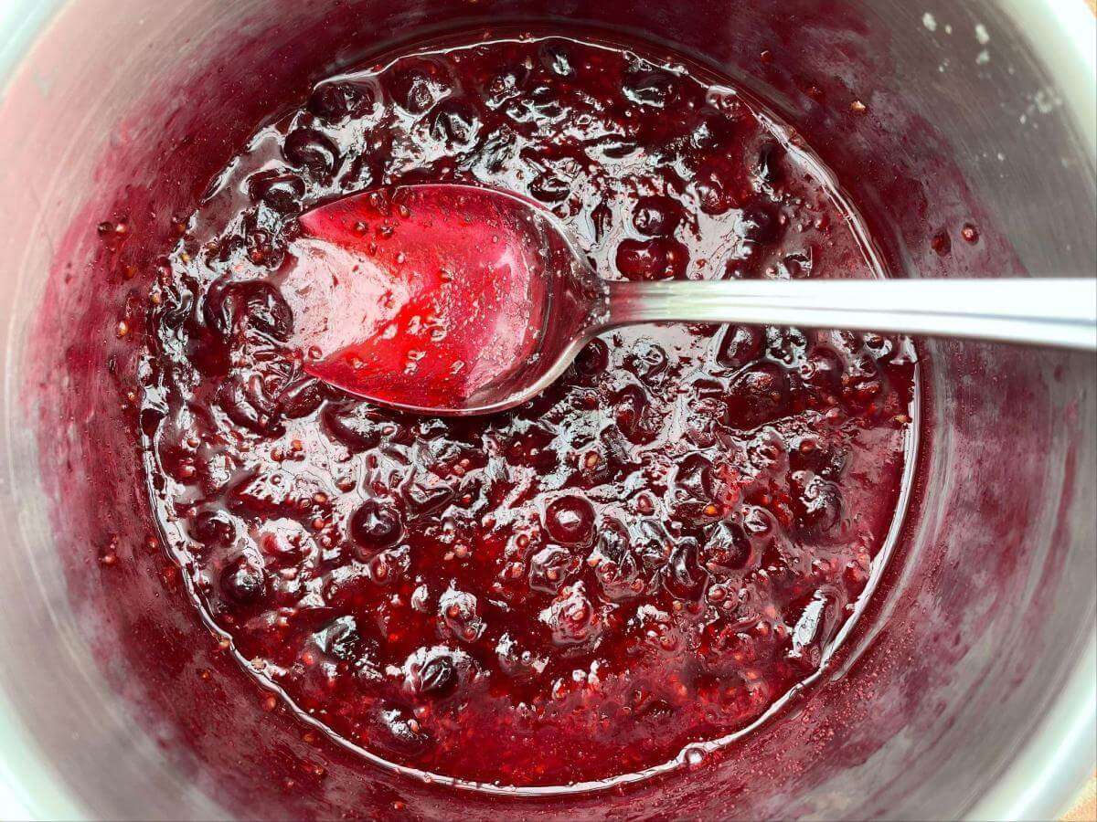 Poached blackcurrants in pan with spoon.