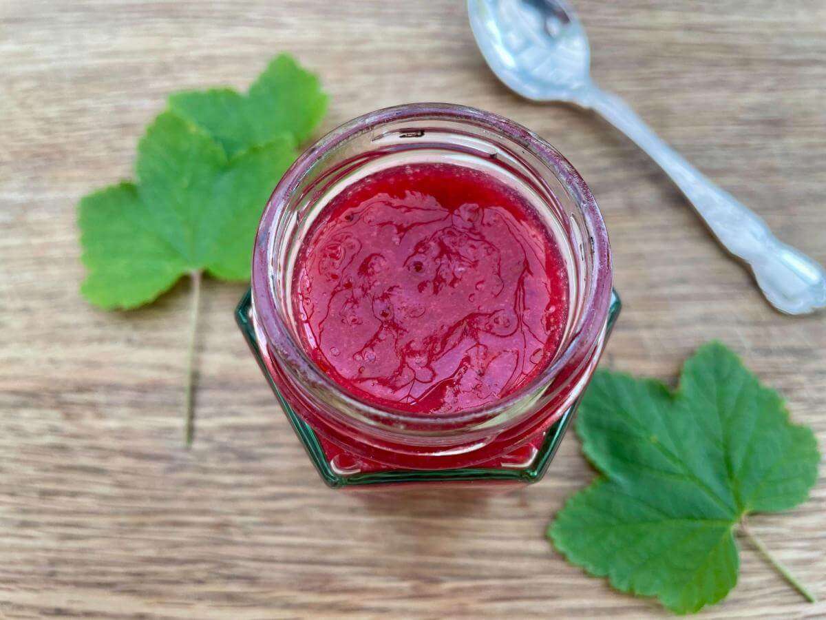 Jar of redcurrant coulis on wooden board.